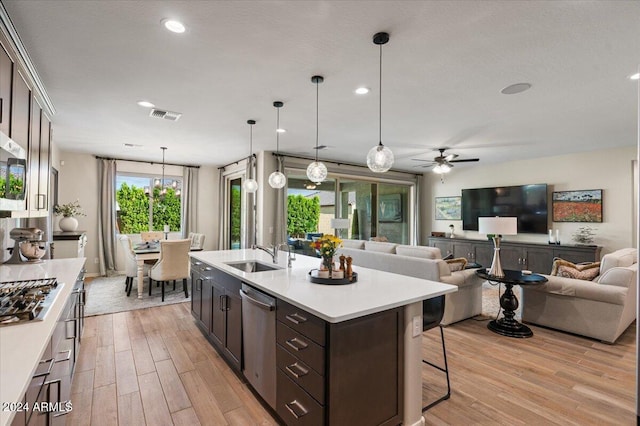 kitchen with light wood-type flooring, dark brown cabinetry, stainless steel appliances, sink, and decorative light fixtures