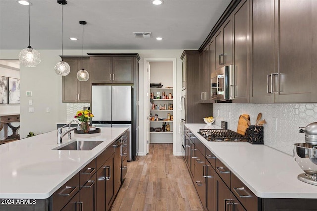 kitchen with sink, hanging light fixtures, light hardwood / wood-style flooring, decorative backsplash, and appliances with stainless steel finishes