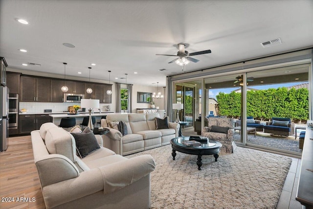 living room featuring ceiling fan with notable chandelier and light wood-type flooring