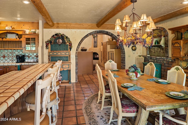 dining area with beam ceiling, dark tile patterned floors, a textured ceiling, and a notable chandelier