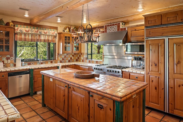 kitchen with sink, tile counters, beamed ceiling, a kitchen island, and appliances with stainless steel finishes