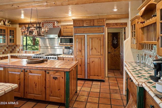 kitchen with tile countertops, sink, a center island with sink, and a notable chandelier