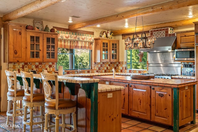 kitchen featuring a center island, an inviting chandelier, tile counters, beam ceiling, and stainless steel appliances