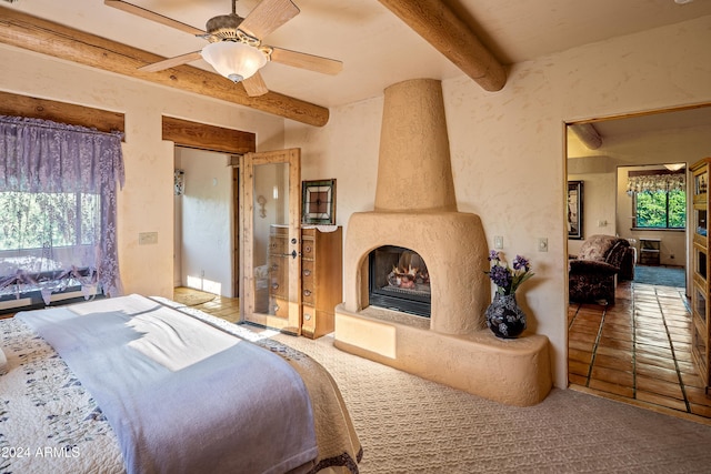 bedroom featuring ceiling fan, beam ceiling, a fireplace, and multiple windows