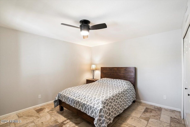 bedroom with a closet, ceiling fan, stone finish flooring, and baseboards