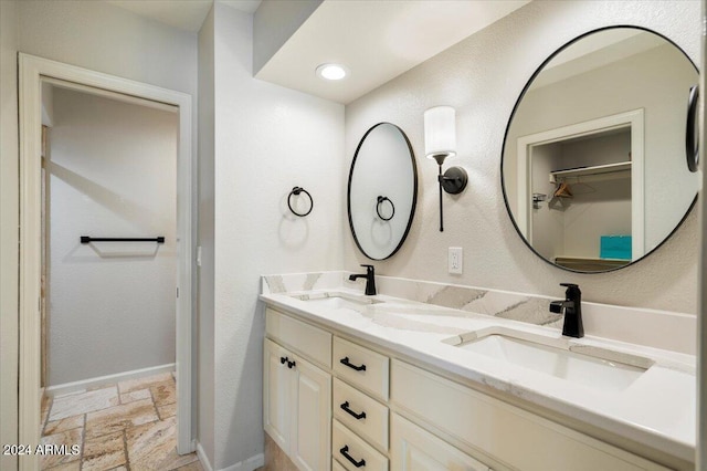 full bath featuring stone tile flooring, double vanity, baseboards, and a sink