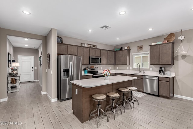 kitchen featuring a breakfast bar, stainless steel appliances, dark brown cabinets, light countertops, and a sink