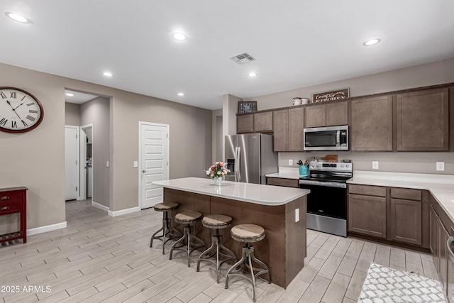 kitchen with stainless steel appliances, visible vents, wood tiled floor, a kitchen island, and a kitchen bar