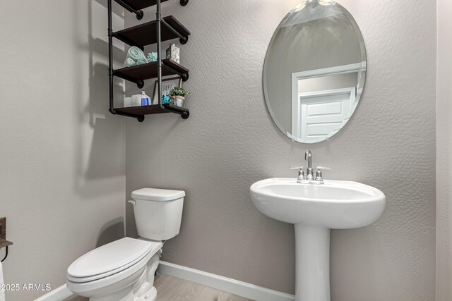 bathroom featuring toilet, a textured wall, baseboards, and wood finished floors