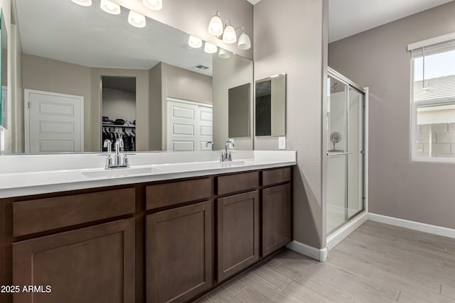 bathroom featuring double vanity, visible vents, a sink, a shower stall, and baseboards