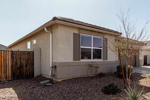 view of side of home with a garage, fence, driveway, and stucco siding