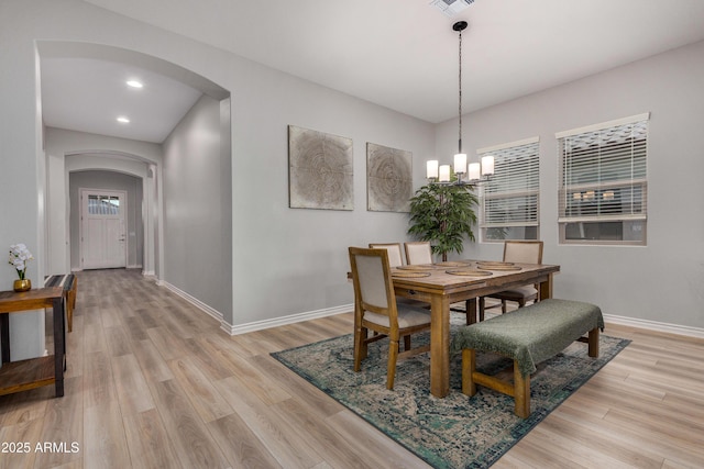 dining area featuring arched walkways, a chandelier, light wood-style flooring, and baseboards