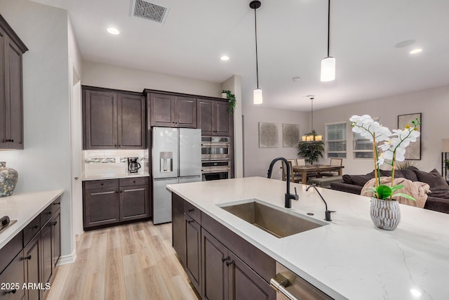 kitchen with pendant lighting, sink, light hardwood / wood-style flooring, dark brown cabinets, and stainless steel appliances