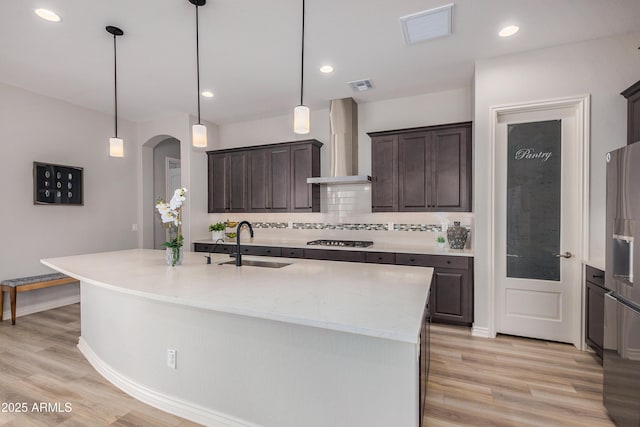 kitchen featuring wall chimney range hood, sink, and a center island with sink