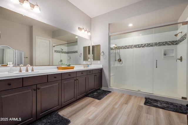 full bath with double vanity, a sink, a stall shower, and wood finished floors