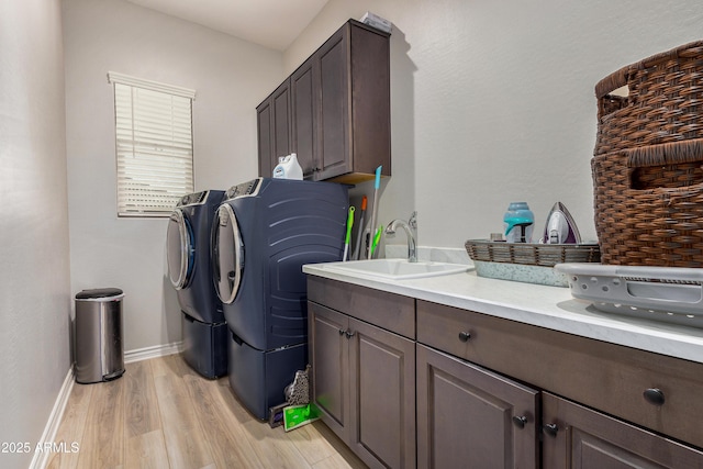 washroom with baseboards, light wood finished floors, cabinet space, a sink, and washing machine and dryer