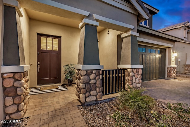 property entrance featuring stone siding, stucco siding, decorative driveway, and a garage