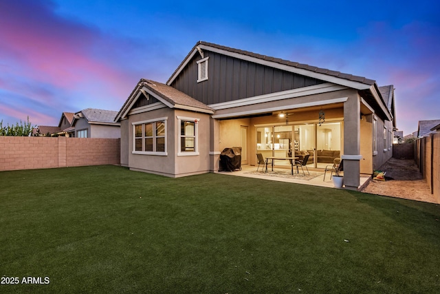 back house at dusk with ceiling fan, a patio, and a lawn