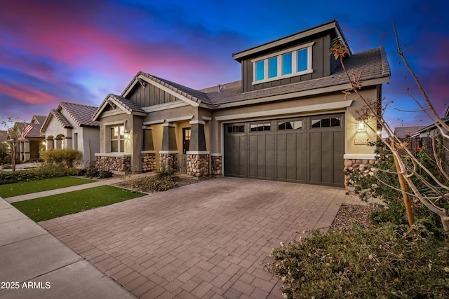 craftsman-style house with stucco siding, a garage, stone siding, a tiled roof, and decorative driveway