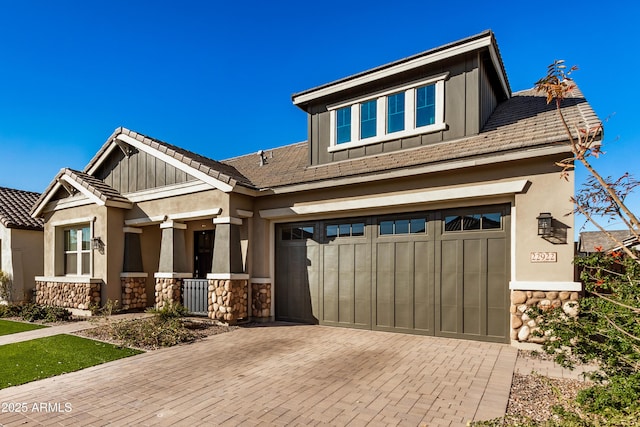 craftsman house with decorative driveway, stone siding, a garage, and board and batten siding