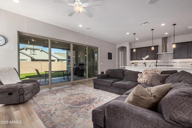 living room featuring light wood-type flooring, visible vents, recessed lighting, arched walkways, and ceiling fan