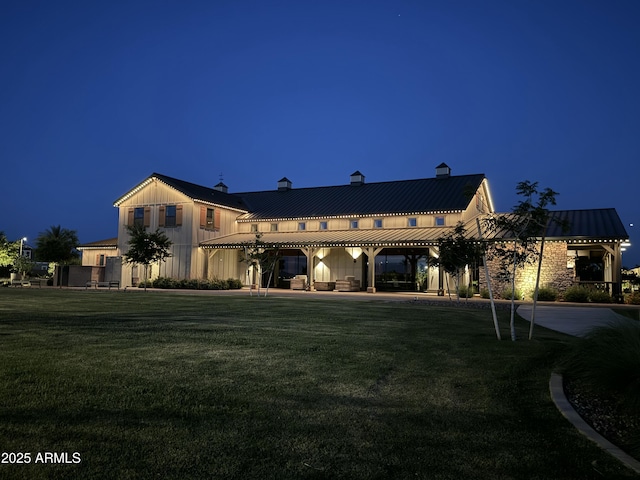 view of front facade featuring a front yard, a standing seam roof, a patio area, board and batten siding, and metal roof