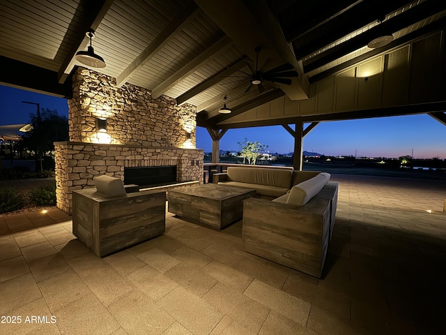 patio terrace at dusk featuring ceiling fan and an outdoor living space with a fireplace