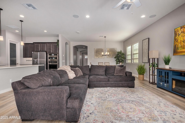 living room featuring ceiling fan with notable chandelier and light wood-type flooring