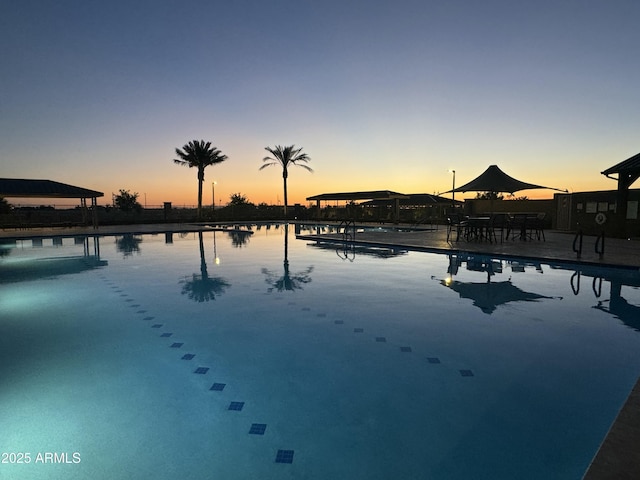 pool at dusk featuring a water view and a patio area