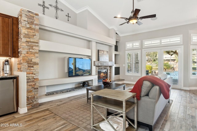 living room featuring crown molding, a stone fireplace, built in features, and light hardwood / wood-style flooring