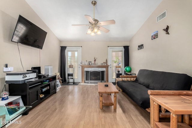 living area featuring light wood finished floors, visible vents, a ceiling fan, a tiled fireplace, and lofted ceiling