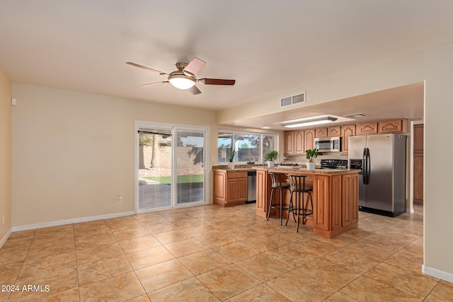 kitchen featuring ceiling fan, a center island, a breakfast bar, appliances with stainless steel finishes, and light tile patterned floors