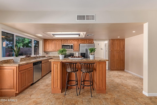 kitchen with sink, light stone counters, appliances with stainless steel finishes, a kitchen bar, and a center island