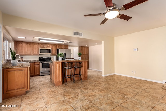 kitchen with ceiling fan, light stone counters, a kitchen island, stainless steel appliances, and a breakfast bar area