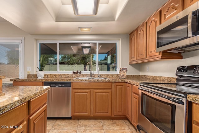 kitchen with a raised ceiling, brown cabinetry, stainless steel appliances, and a sink