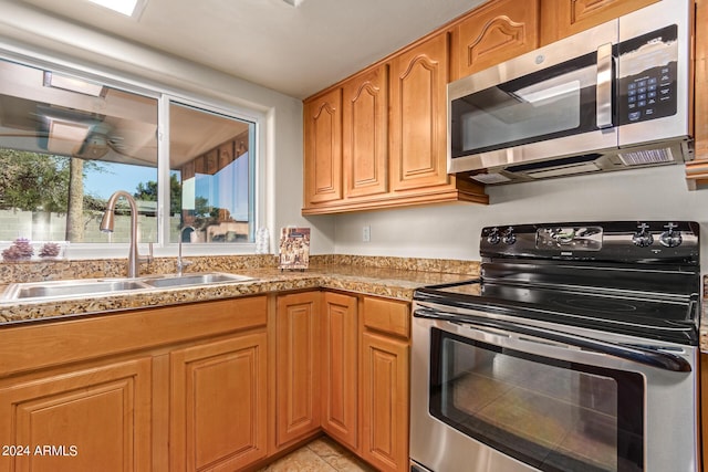 kitchen featuring brown cabinets, light countertops, light tile patterned floors, a sink, and appliances with stainless steel finishes