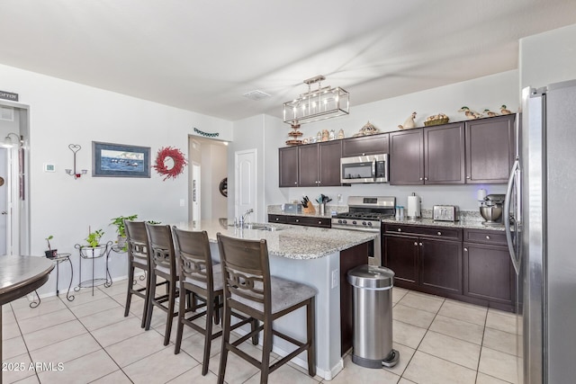 kitchen featuring appliances with stainless steel finishes, a breakfast bar, dark brown cabinetry, and light tile patterned floors