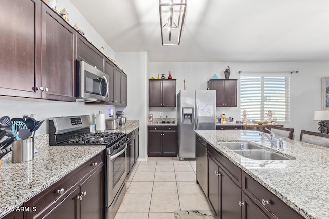 kitchen with dark brown cabinetry, light stone counters, stainless steel appliances, a sink, and light tile patterned flooring