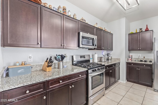 kitchen featuring stainless steel appliances, light tile patterned floors, dark brown cabinetry, and light stone countertops