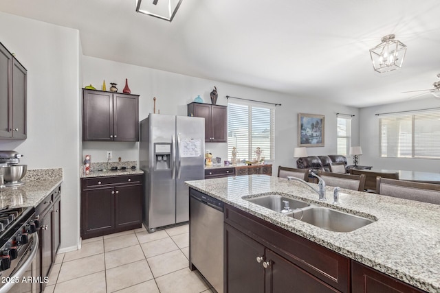 kitchen featuring dark brown cabinetry, light tile patterned floors, open floor plan, stainless steel appliances, and a sink