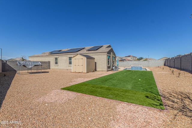 rear view of house featuring an outbuilding, a lawn, a storage shed, roof mounted solar panels, and a fenced backyard