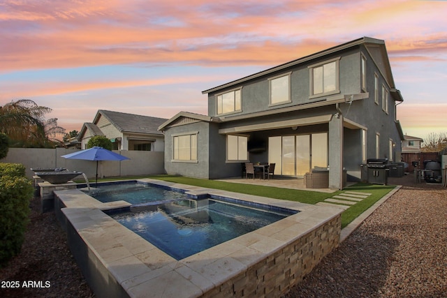 back house at dusk with a patio and an in ground hot tub