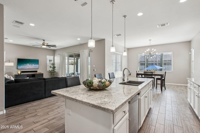 kitchen with hanging light fixtures, white cabinetry, a kitchen island with sink, and sink