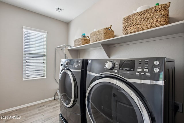 clothes washing area with washer and clothes dryer and light wood-type flooring