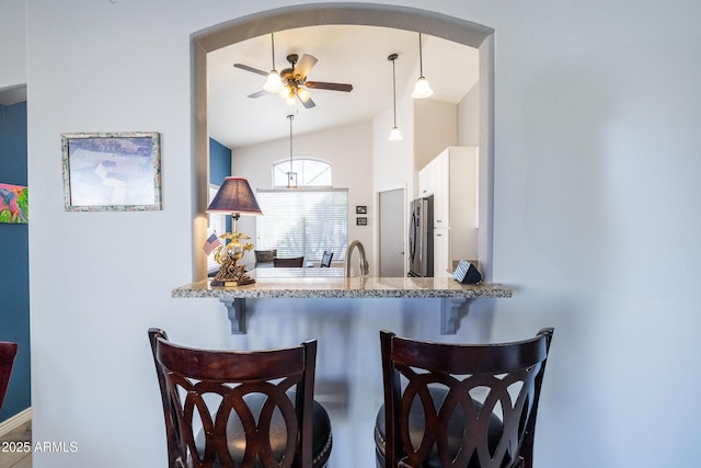 kitchen with light stone counters, decorative light fixtures, lofted ceiling, stainless steel refrigerator, and ceiling fan