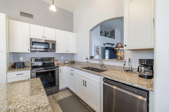 kitchen featuring appliances with stainless steel finishes, light wood-type flooring, white cabinets, decorative light fixtures, and sink