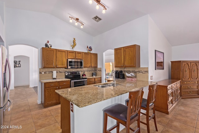 kitchen with kitchen peninsula, appliances with stainless steel finishes, high vaulted ceiling, a kitchen bar, and sink