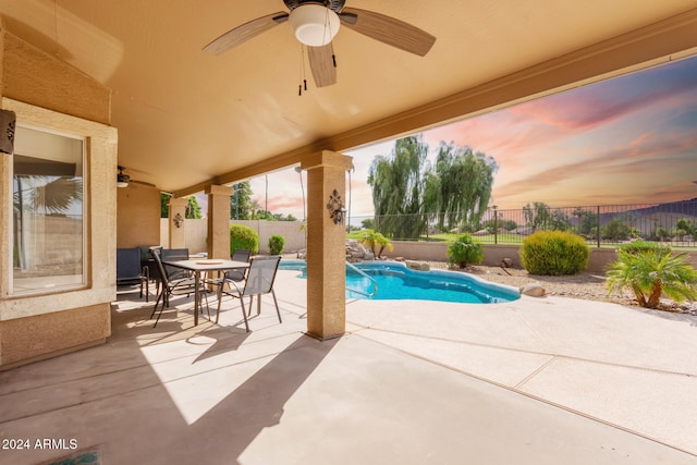 pool at dusk with ceiling fan and a patio area