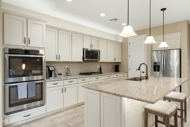 kitchen with a breakfast bar, a sink, hanging light fixtures, stainless steel appliances, and backsplash