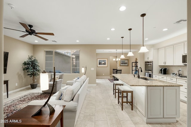 kitchen with stainless steel appliances, visible vents, open floor plan, tasteful backsplash, and an island with sink